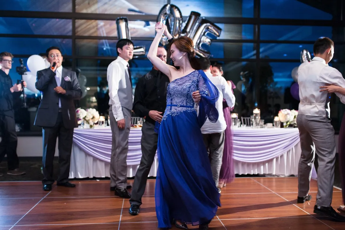 A smiling woman in a blue dress turning with her partner at a celebration