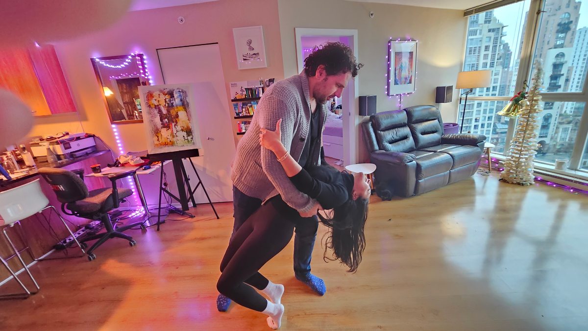 Two partners practicing a supported dip in a purple-lit room